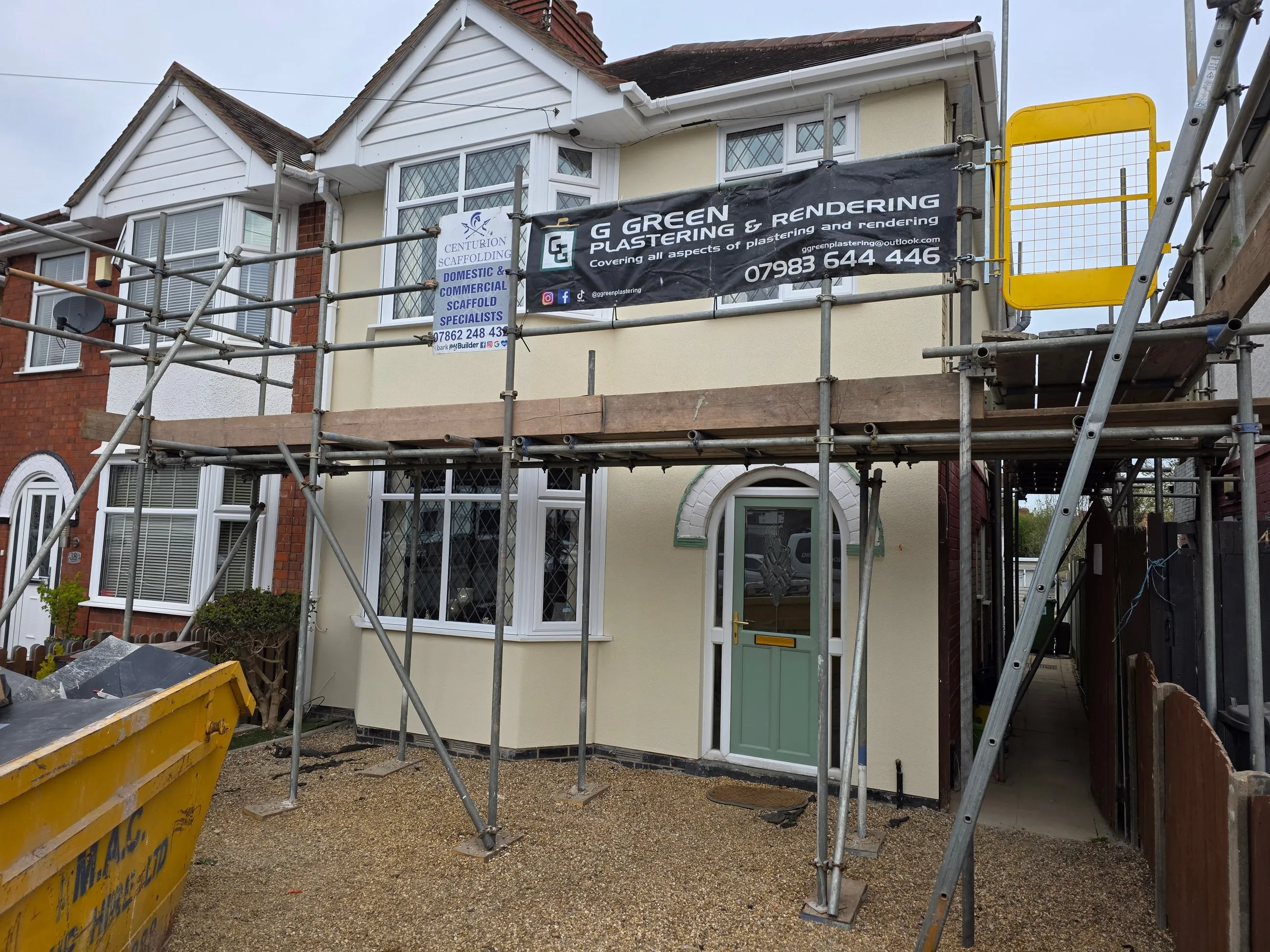 A semi-detached house part-way through rendering, scaffolding across the front and a G Green Plastering & Rendering banner fixed to it.